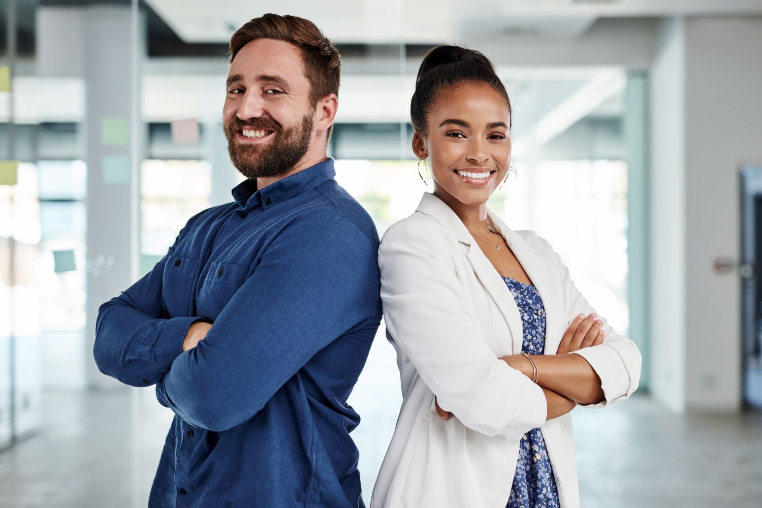man and woman back to back, posing with arms crossed in an office